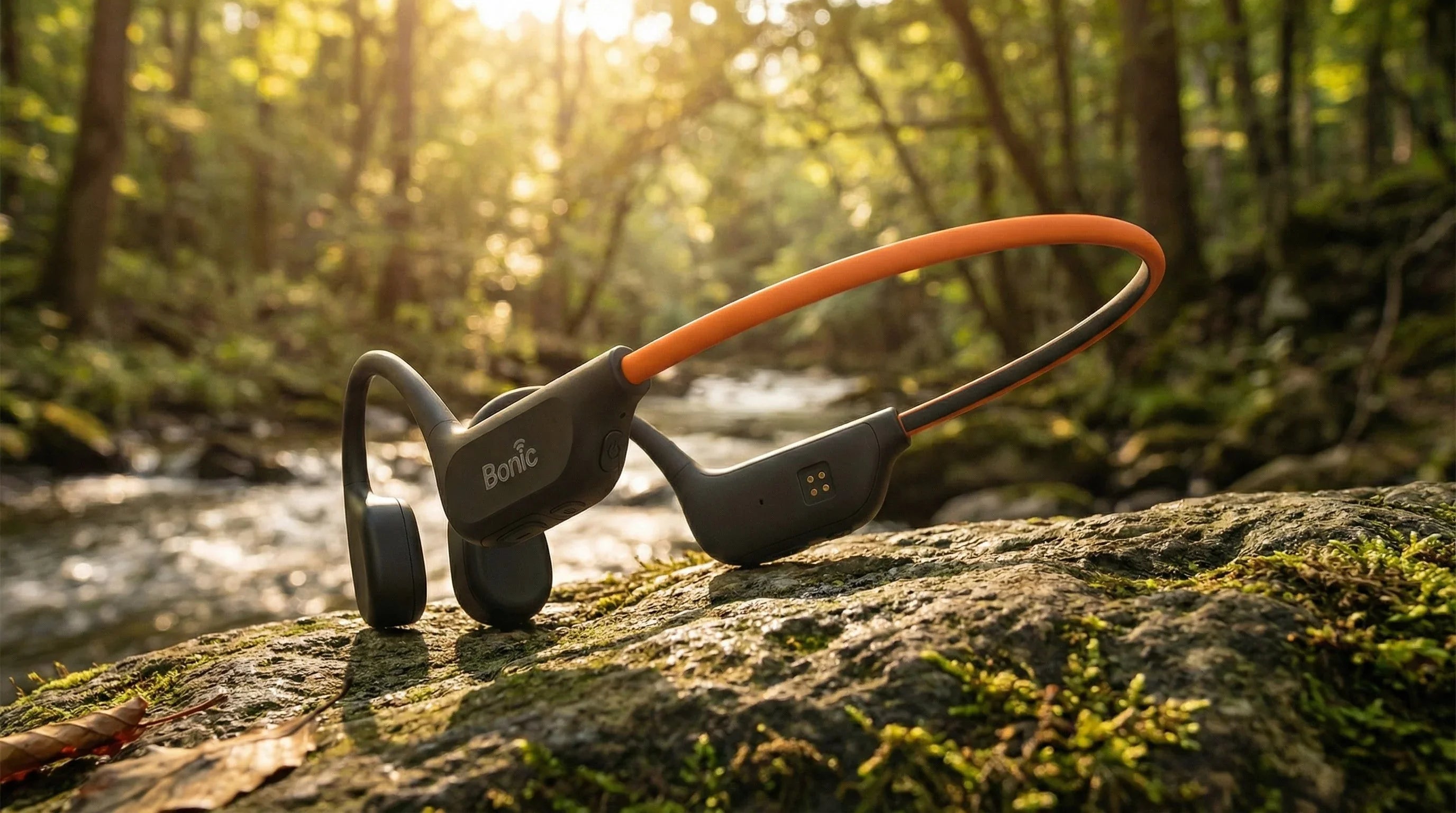 Bonic black and orange bone conduction headphones resting on mossy rock in forest with sunlight